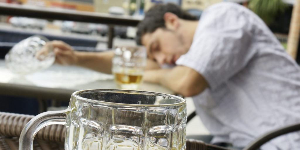 Alcohol abuse: drunk young man or student lying down on a table with beer bock still in hand, focus on glass up front.