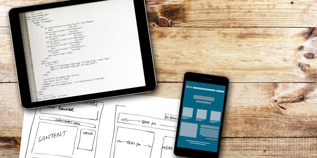 website wireframe sketch and programming code on digital tablet